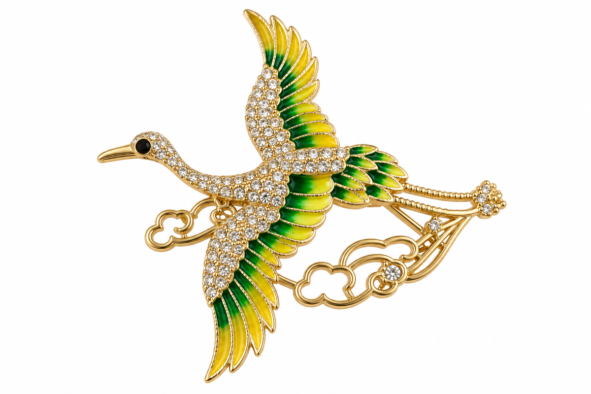 Flying crane brooch with green and yellow wings and sparkling crystal-style stones on white background